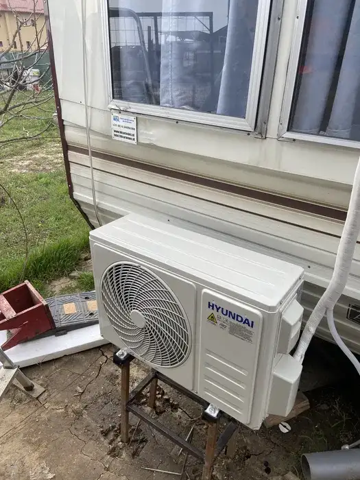 Unitatea exterioară Hyundai pe suport metalic la sol, lângă rulotă